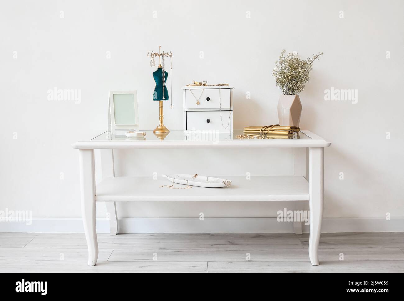 Gioielli alla moda, vaso con fiori e cornice fotografica sul tavolo vicino alla parete bianca Foto Stock