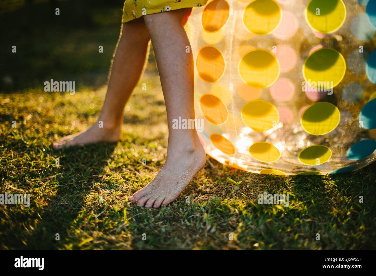 Piedi di sabbia per bambini su erba verde con pallina arcobaleno e luce dorata Foto Stock