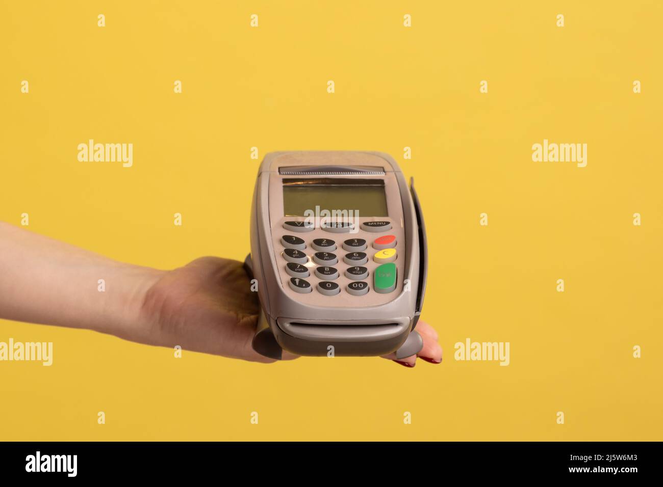 Vista laterale del profilo primo piano della mano della donna e che mostra il pagamento POS o terminale o il dispositivo pay pass. Studio interno girato isolato su sfondo giallo. Foto Stock