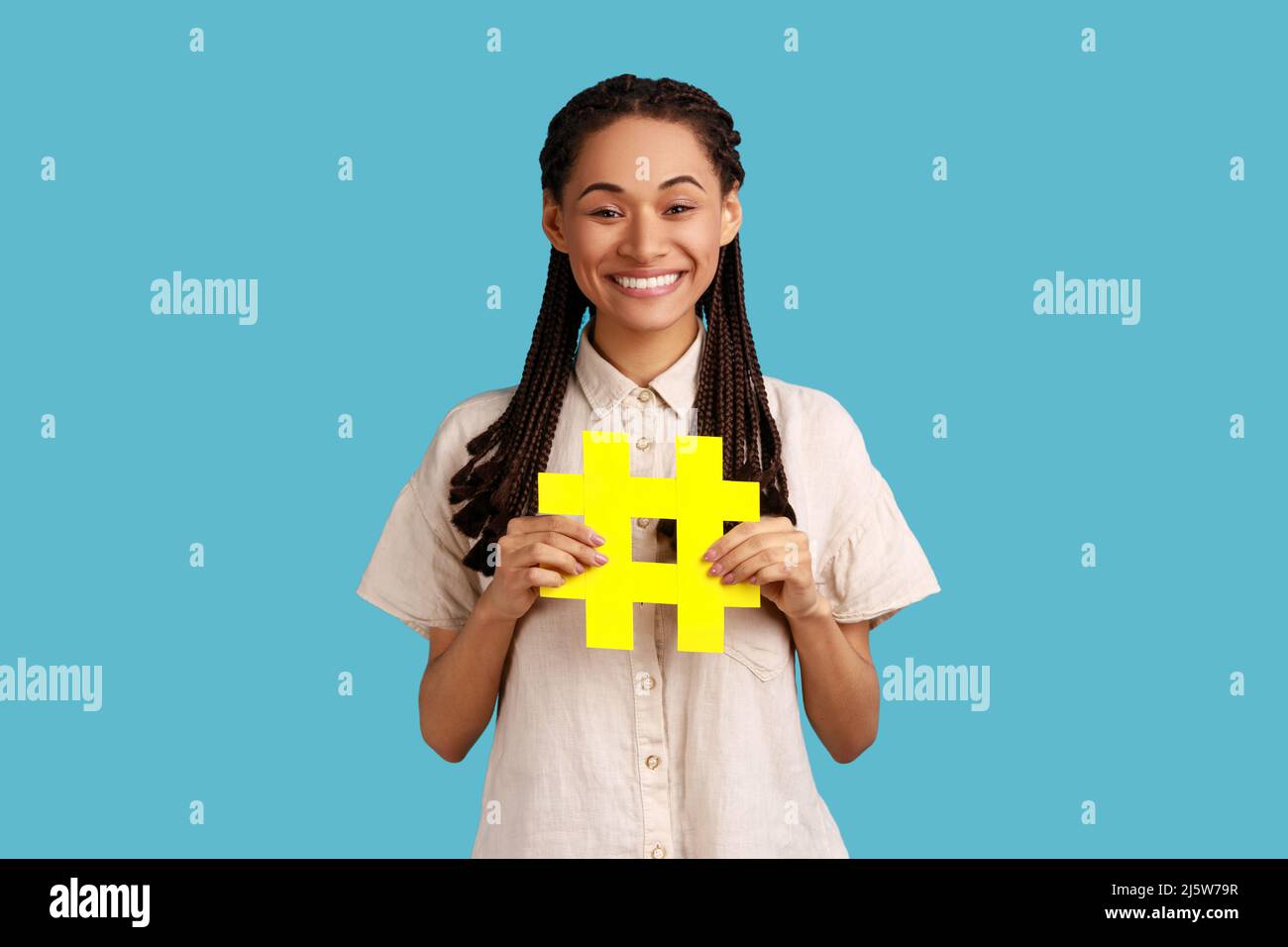 Popolarità del Internet. Ritratto di donna felice con i readlocks neri che tengono hashtag simbolo, promuovendo il tema virale nel social network, tagging blog tendenze. Studio interno girato isolato su sfondo blu. Foto Stock