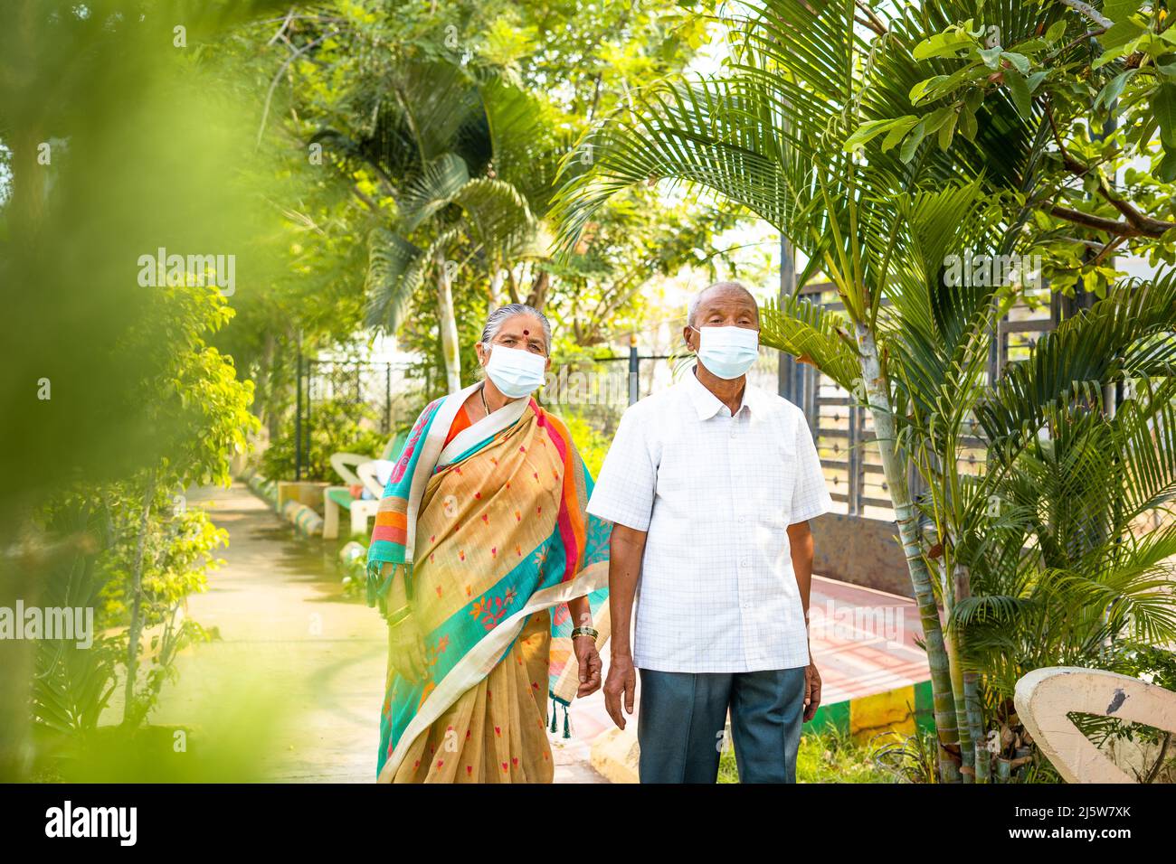 Coppie anziane con maschera medica durante la passeggiata mattutina al parco - concetto di covid-19 protezione del coronavirus, salute e sicurezza. Foto Stock