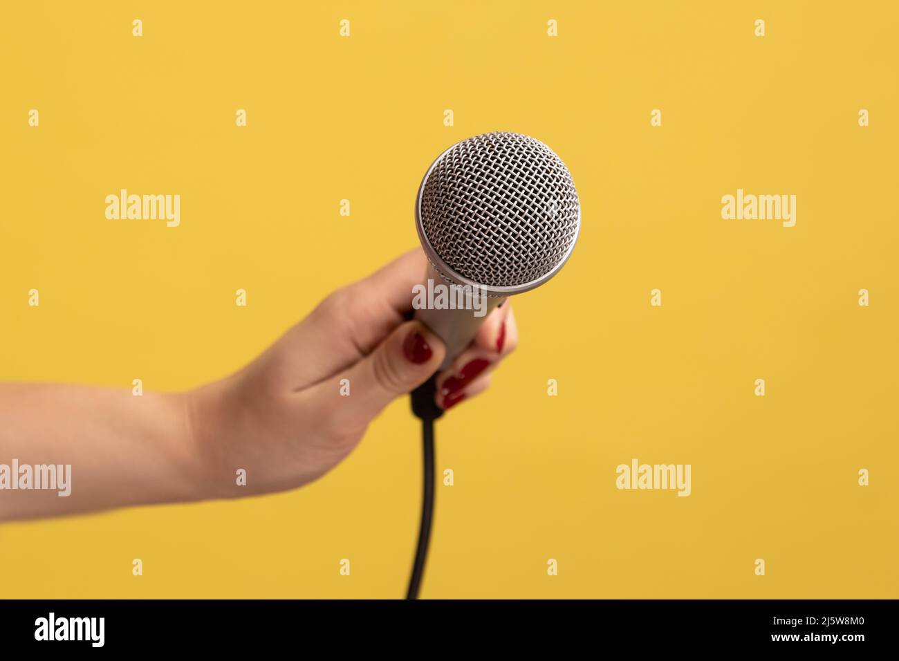 Ritratto closeup di donna mano tenendo microfono, si riferisce alla risposta np domanda. Studio interno girato isolato su sfondo giallo. Foto Stock