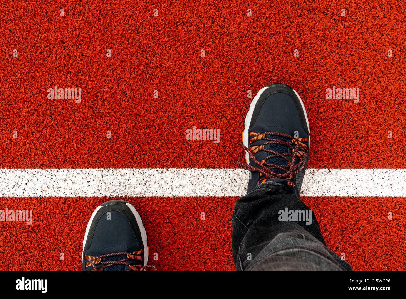 I piedi da uomo in sneakers nere si levano in pista, un piede ha fatto un passo su una linea bianca.camminando attraverso la linea di partenza che rappresenta l'inizio di affari e di vita Foto Stock