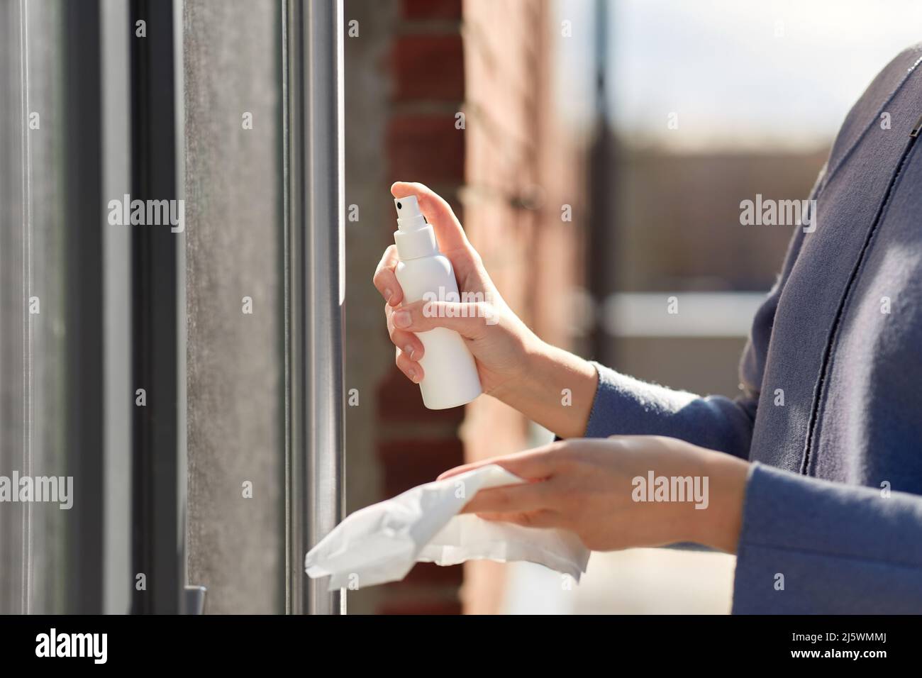 donna pulizia maniglia porta con disinfettante spray Foto Stock