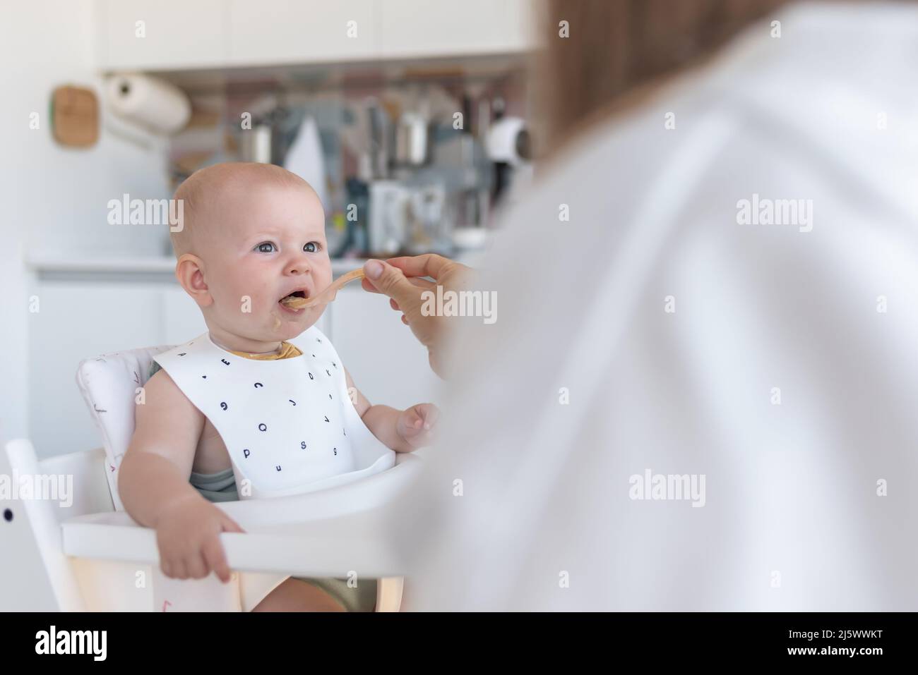 la prima alimentazione del bambino, la madre nutre il bambino nella cucina Foto Stock