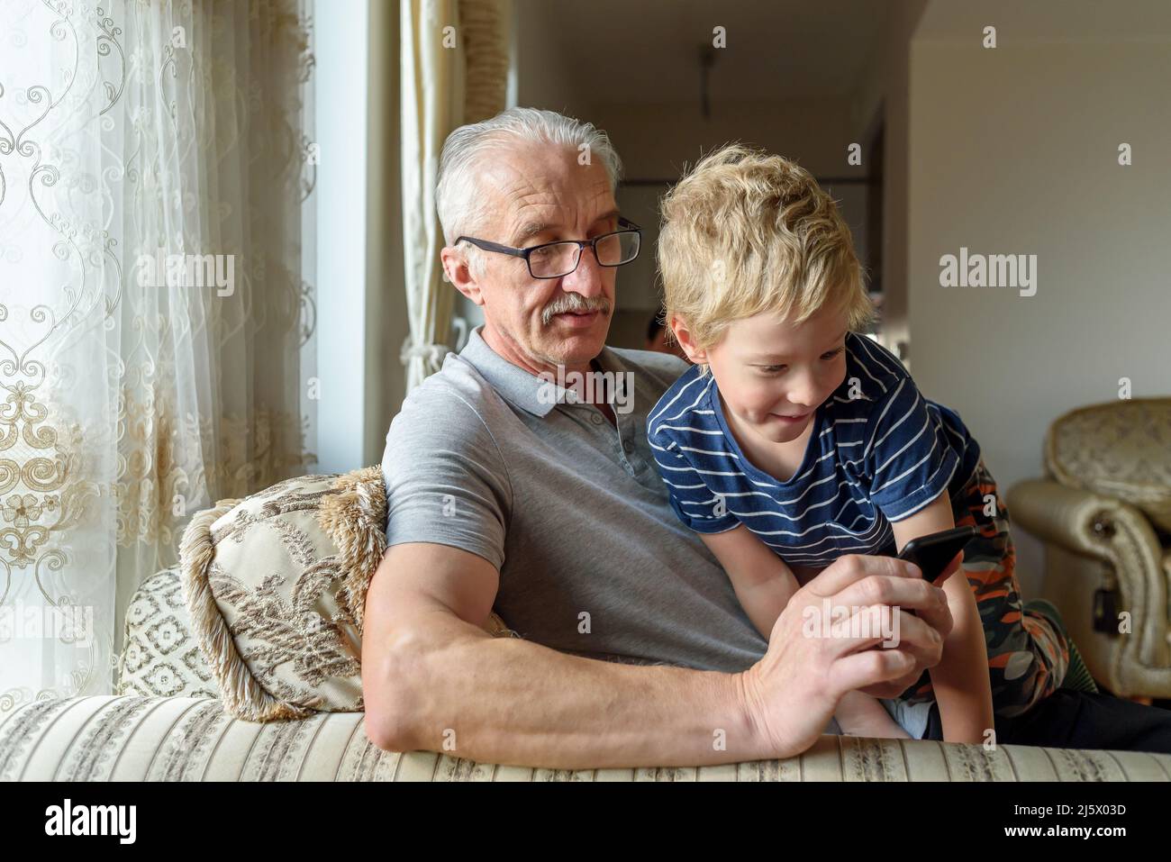 Nonno con nipote che usa il telefono cellulare. Guardare video, chiamare Foto Stock