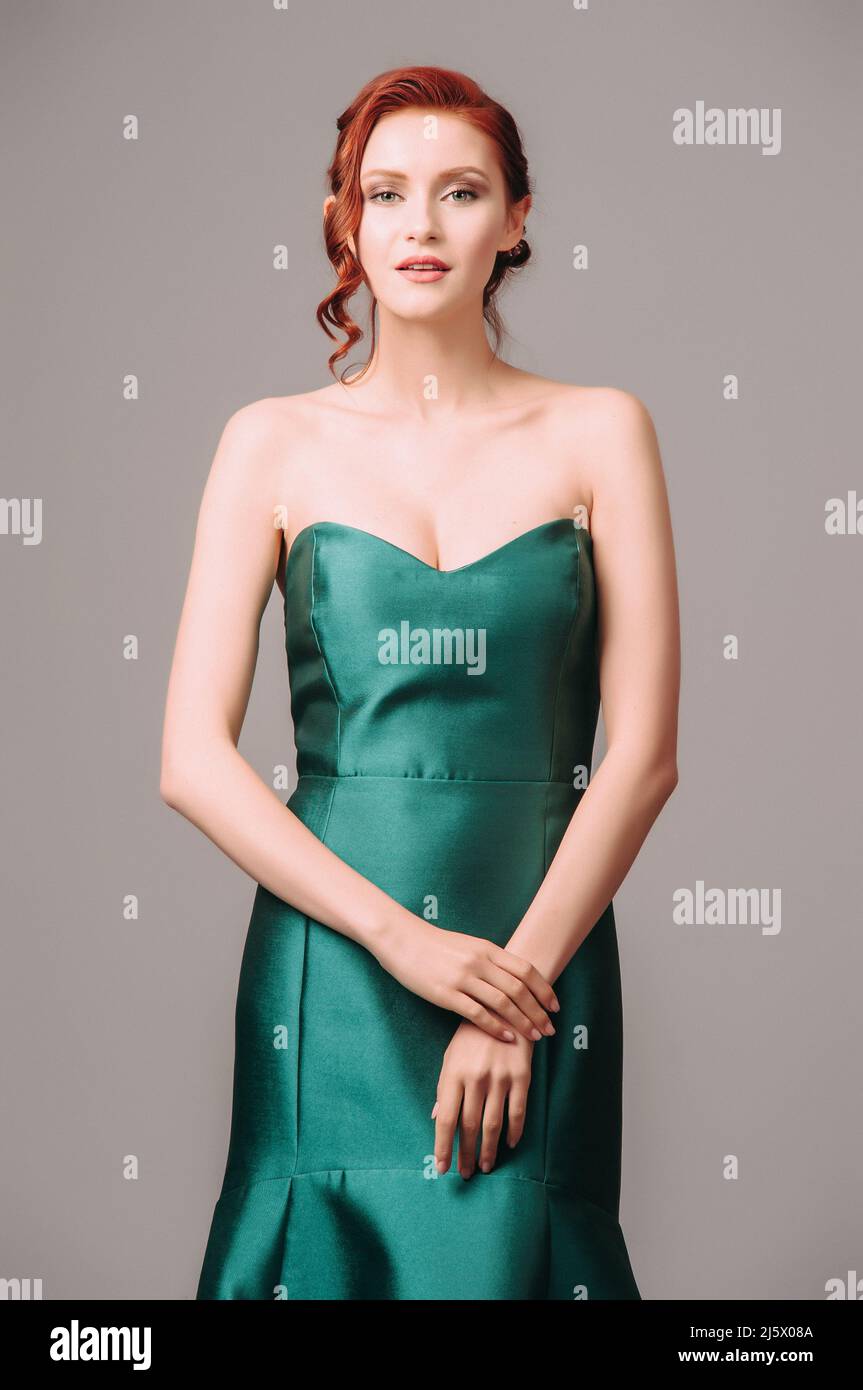 Abito da palla smeraldo. Giovane donna in abito da sera verde lungo. Donna zenzero in posa in studio. Bel modello con tacco alto, look femminile per una vigilia Foto Stock