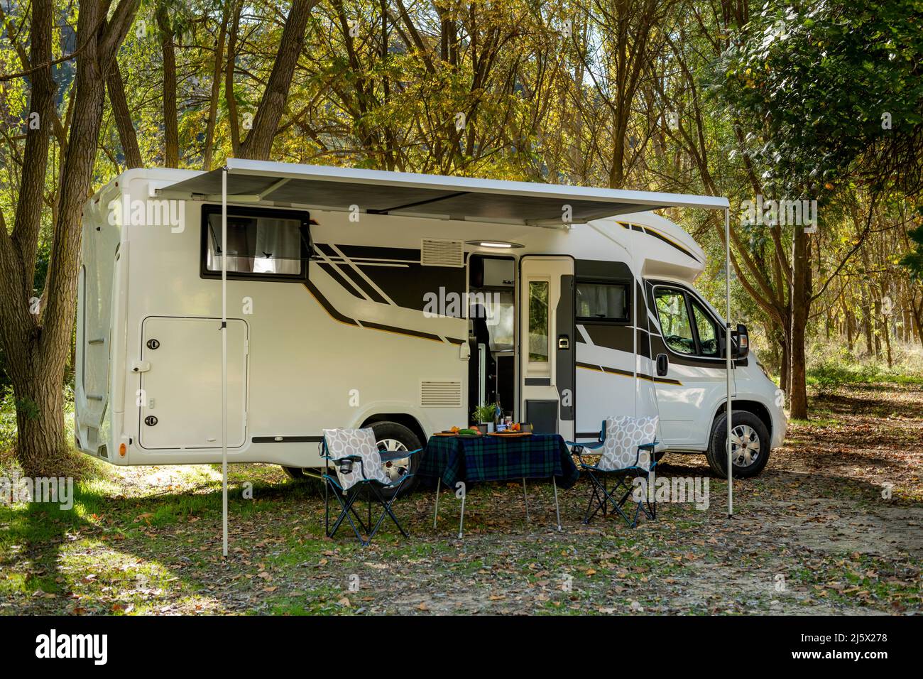 Casa a motore in campeggio con un tavolo e sedie allestiti all'esterno del veicolo e pronti a mangiare e bere. Foto Stock