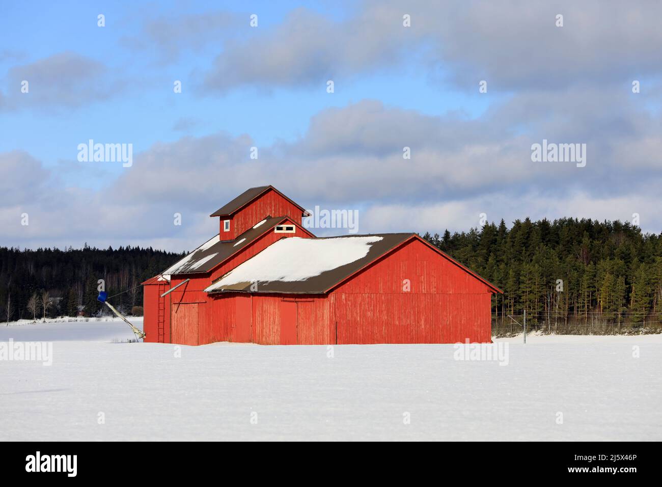 Rosso, vecchio essiccatore di grano di legno in campo in un giorno limpido di febbraio con campo coperto di neve e cielo blu e nuvole. Foto Stock