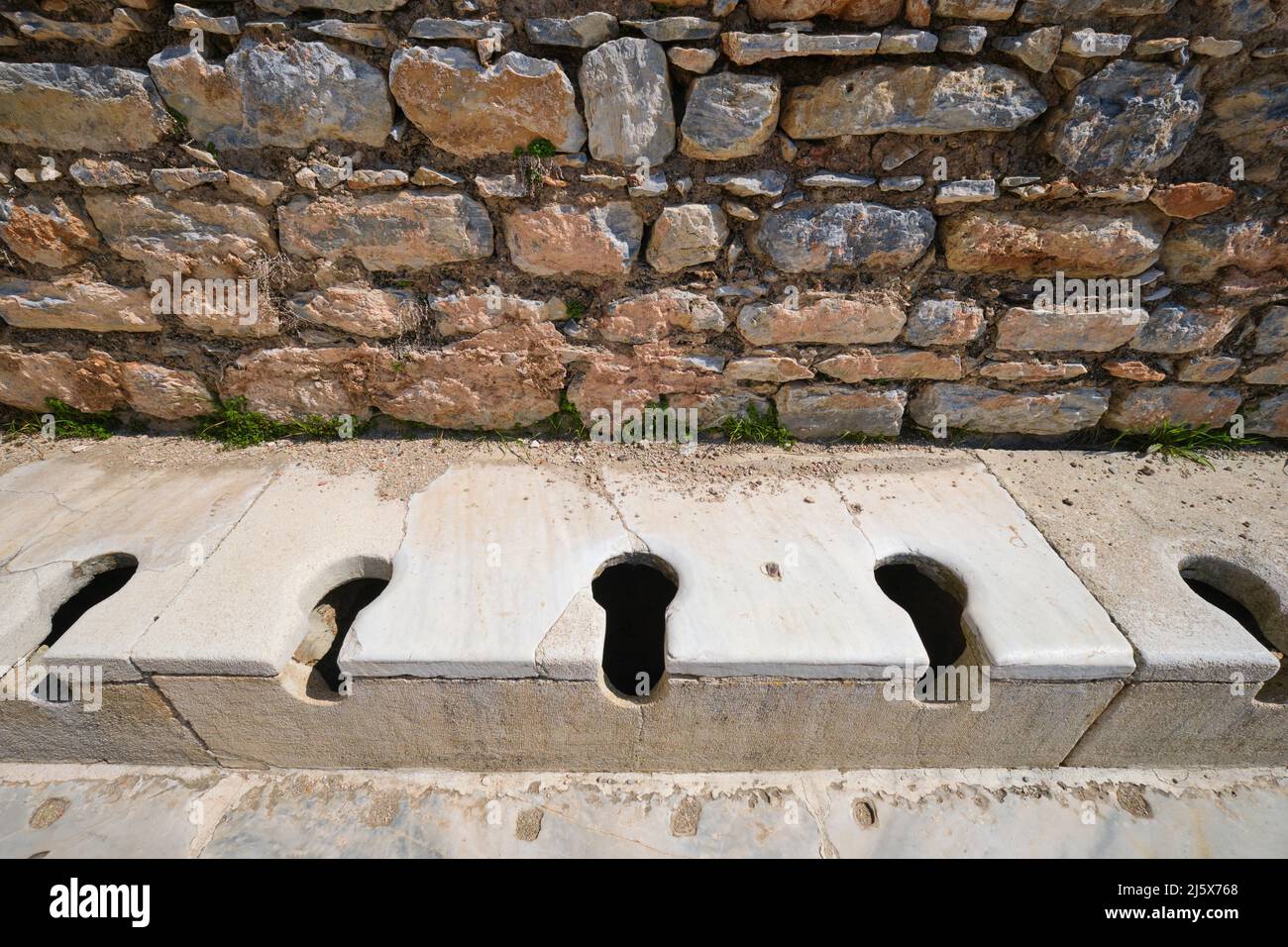 Una vista di una serie di panca, wc in pietra, fori bagno presso l'edificio latrine. Presso l'antico greco, sito archeologico romano Efeso. A İ Foto Stock
