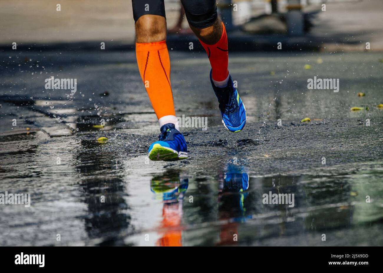 gambe atleta maschile in calze a compressione che corre su strada bagnata Foto Stock