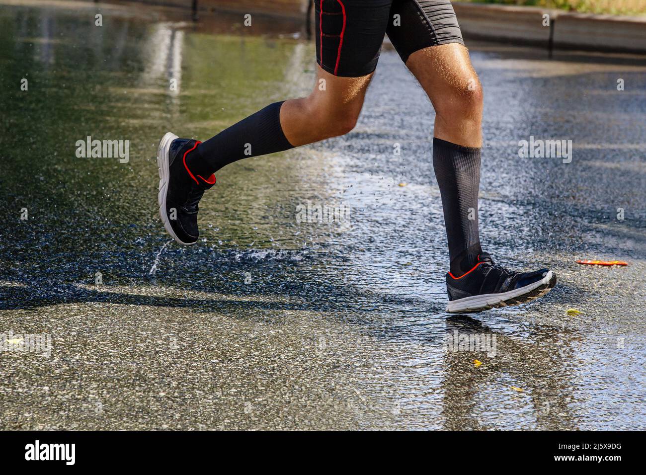 gambe uomo runner in calze a compressione running su asfalto bagnato Foto Stock