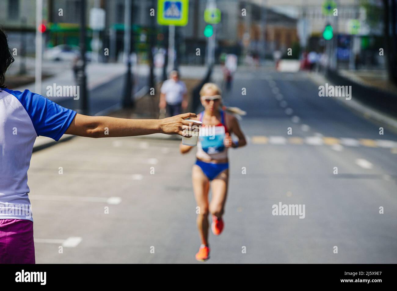 il volontario dà acqua in vetro alla maratona di corsa dell'atleta femminile Foto Stock