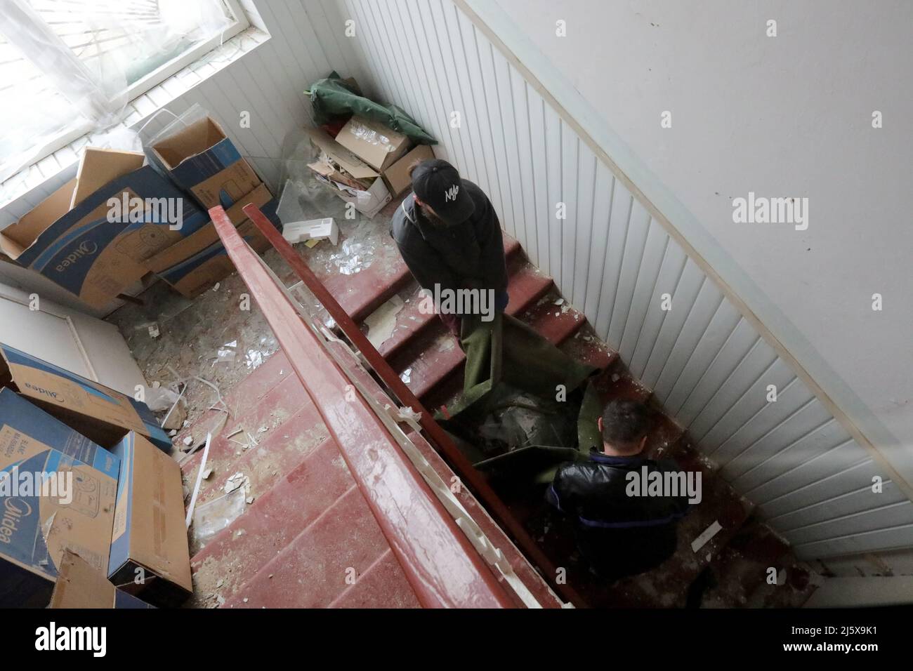 BORODIANKA, UCRAINA - 26 APRILE 2022 - gli uomini trasportano le protezioni di vetro giù le scale in un centro di risorse inclusive danneggiato durante l'invasione russa durante r Foto Stock