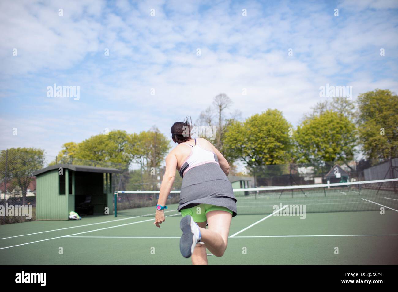 Donna che gioca a tennis su un campo da tennis soleggiato Foto Stock