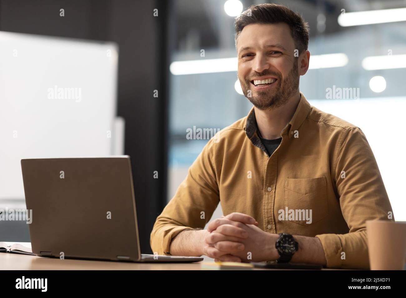 Uomo imprenditore felice vicino computer portatile in posa in ufficio moderno Foto Stock