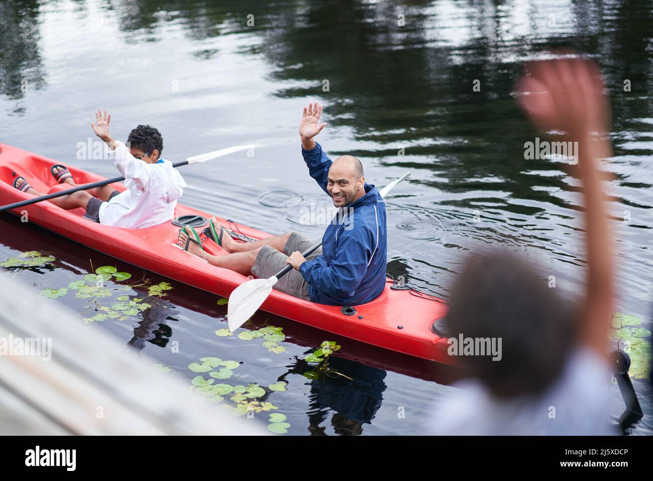 Buon padre e figlio che sventolano dal kayak sul fiume Foto Stock