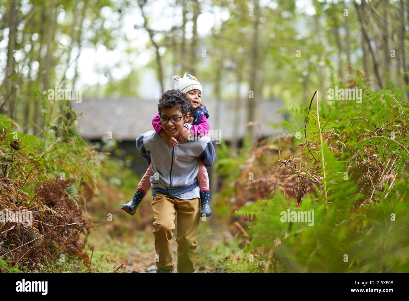Fratello suora piggybacking su sentiero in boschi Foto Stock