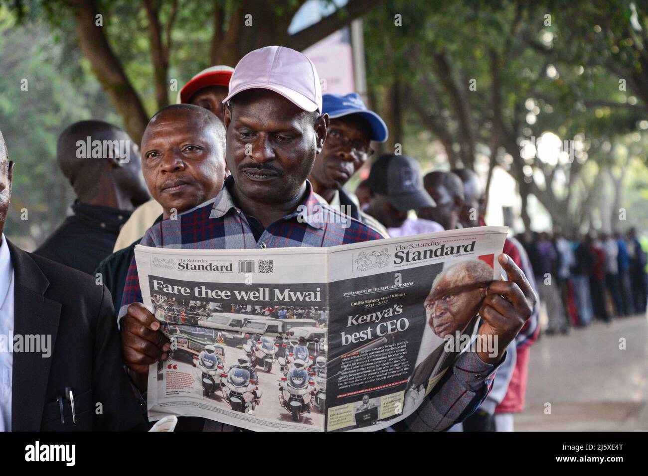 Nairobi, Kenya. 25th Apr 2022. Un membro del pubblico legge un giornale che riferisce sulla morte dell'ex presidente del Kenya Mwai Kibaki mentre si accoda per vedere il suo corpo che si trova nello stato per il secondo giorno presso il Parlamento. L'ex capo di stato, che governò per otto anni (dal 2002 dicembre al 2013 aprile) morì il 22 aprile 2022, come annunciato dall'attuale presidente Uhuru Kenyatta. Credit: SOPA Images Limited/Alamy Live News Foto Stock