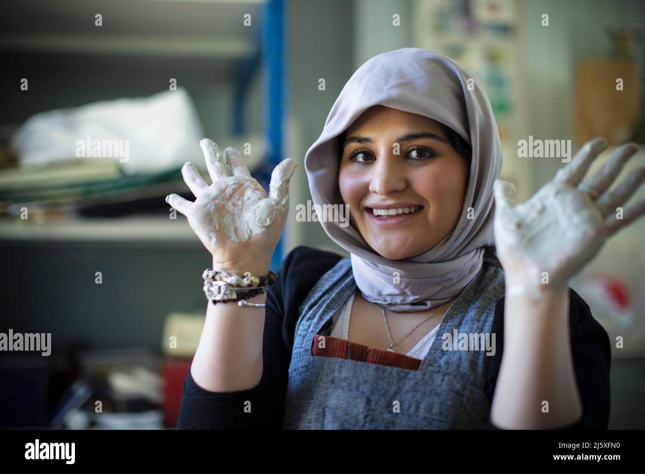 Ritratto felice giovane artista femminile in hijab con mani coperte di argilla Foto Stock