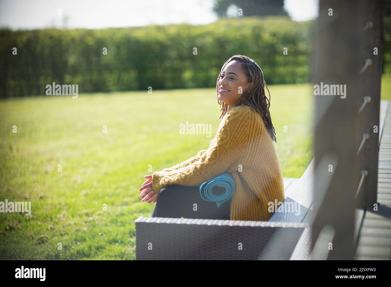 Giovane donna felice con tappeto yoga su panca soleggiata Foto Stock