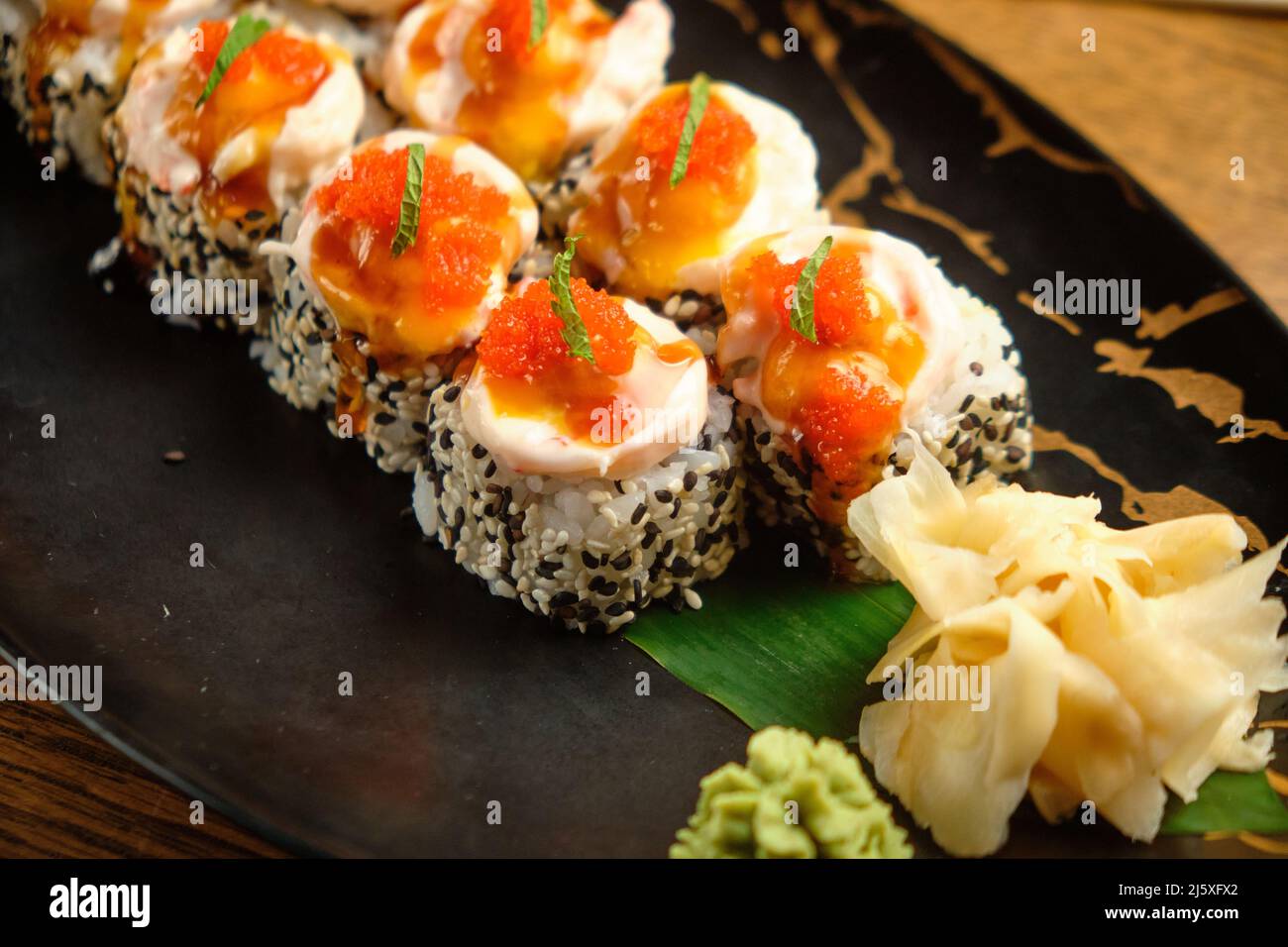 Una serie di sushi roll con salmone, caviale, avocado e sesamo nero in primo piano. Fuoco selettivo Foto Stock