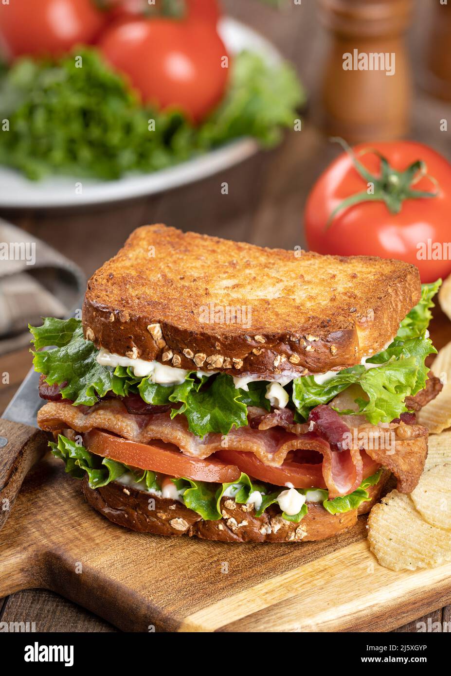 Panino BLT con pancetta, lattuga e pomodoro su pane tostato a grani interi su un tagliere di legno Foto Stock