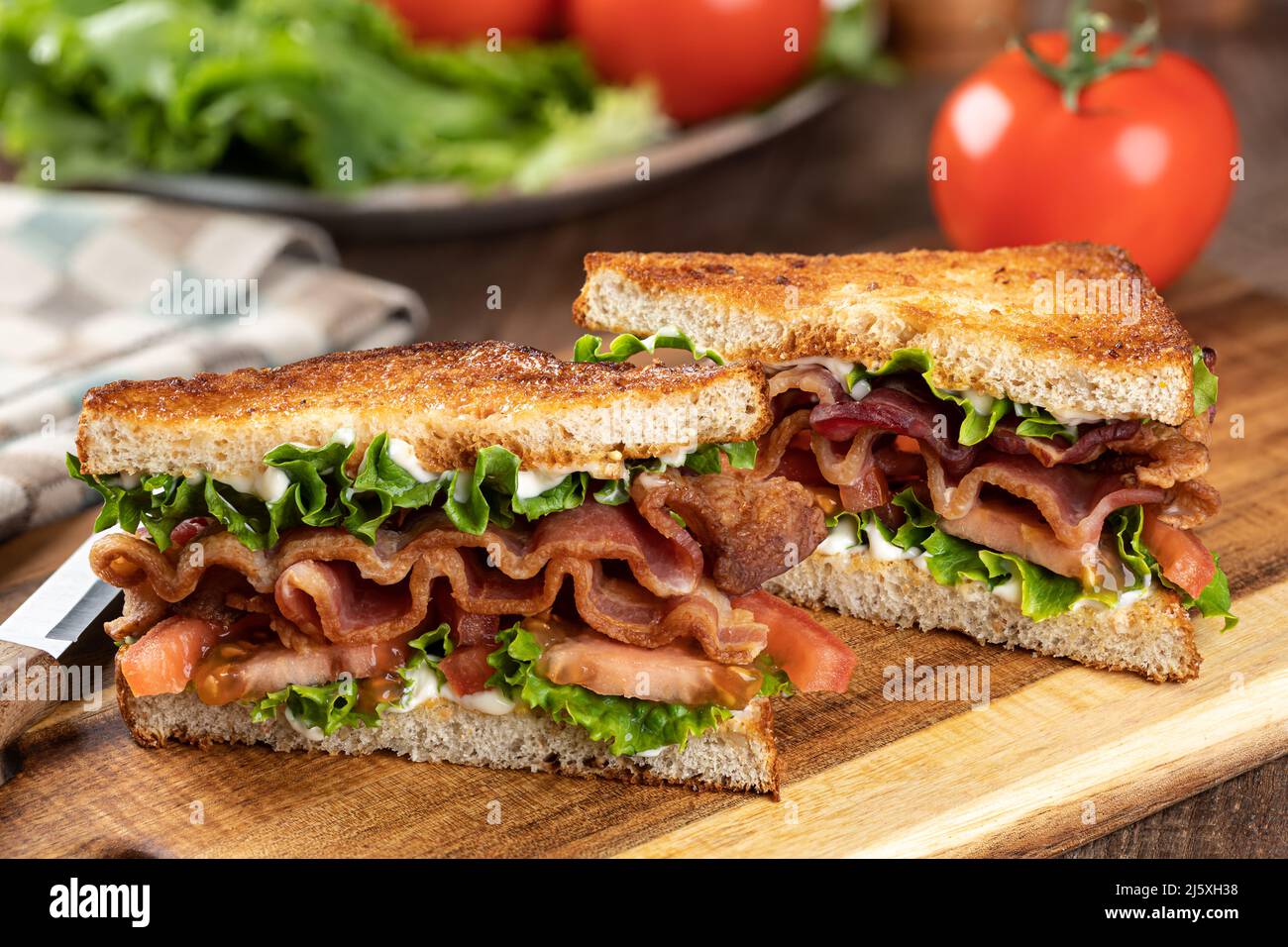 Panino BLT fatto con pancetta, lattuga e pomodoro su pane tostato a grani interi tagliato a metà su un tagliere di legno Foto Stock