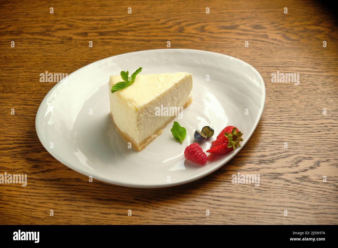 Un pezzo di cheesecake, una classica cheesecake in stile New York su un tavolo di legno Un pezzo di deliziosa torta su un piatto bianco Foto Stock