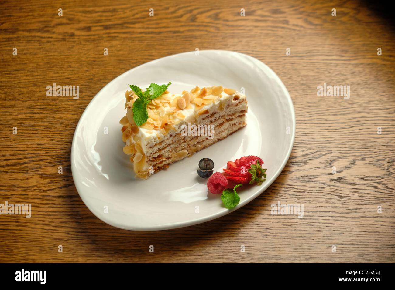 Fake a strati con panna Napoleone Slice su un piatto bianco con fragole su un tavolo di legno Foto Stock