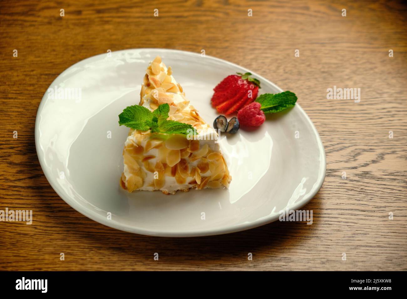 Fake a strati con panna Napoleone Slice su un piatto bianco con fragole su un tavolo di legno Foto Stock