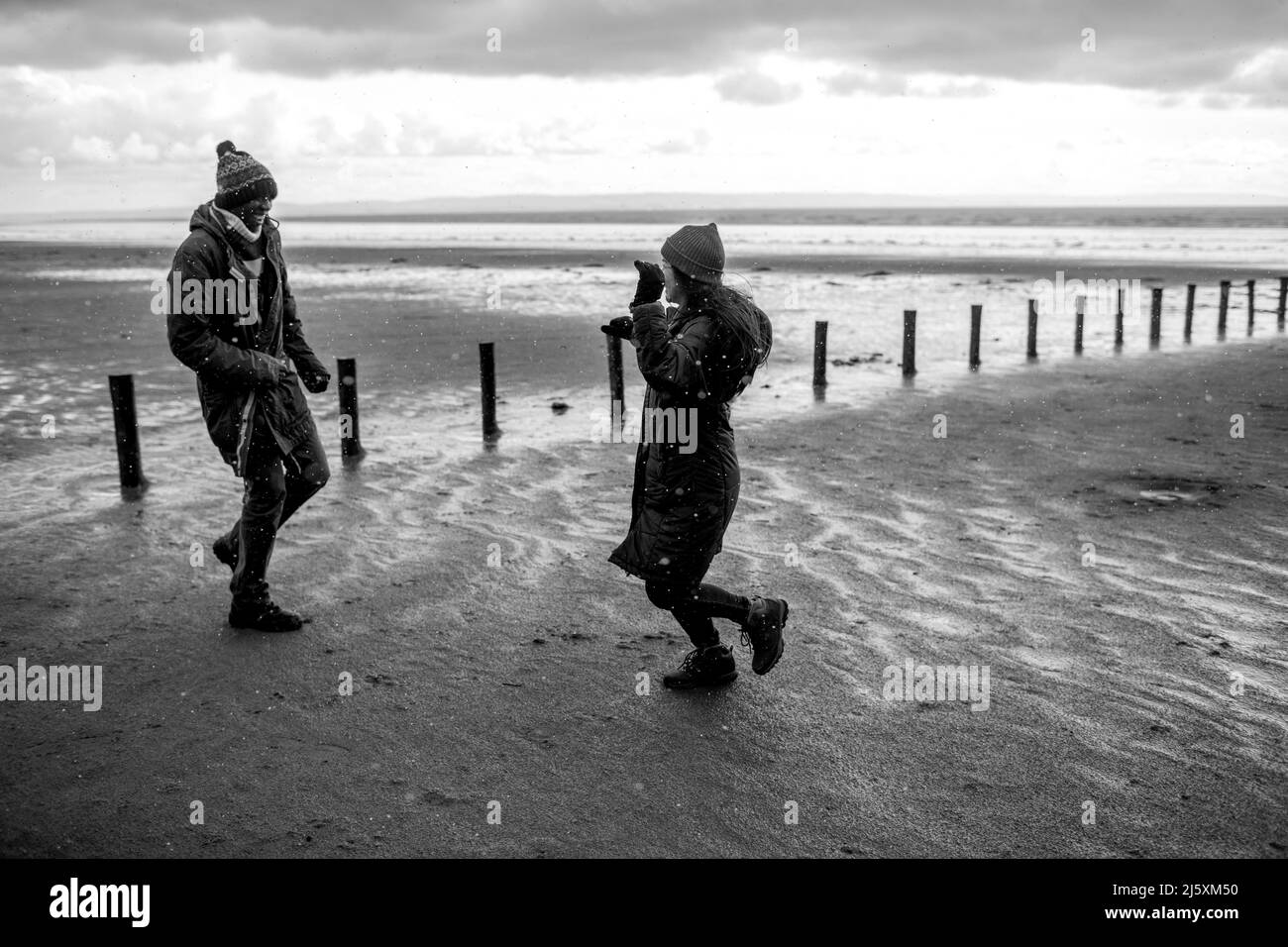 Coppia giocosa che corre sulla spiaggia bagnata d'inverno Foto Stock