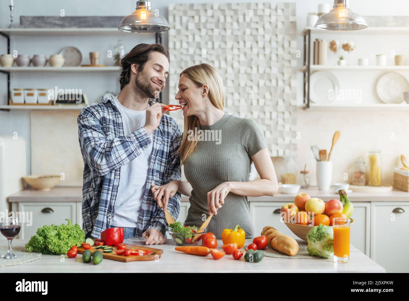 Felice giovane marito europeo con stubble nutre donna, signora prepara insalata per la cena Foto Stock