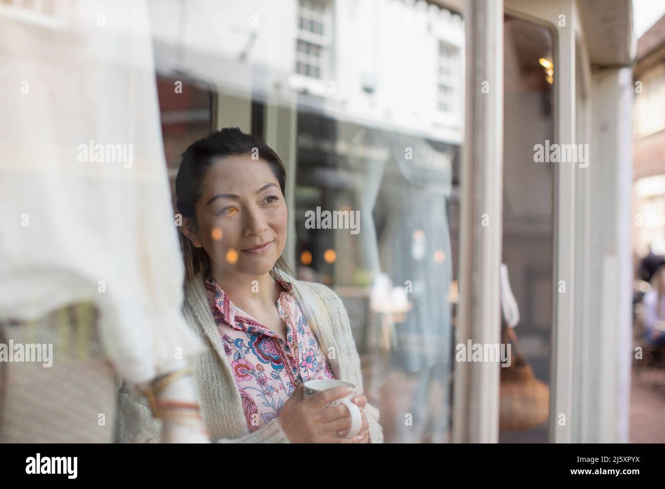 Donna proprietario del negozio che beve il tè alla vetrina del negozio Foto Stock