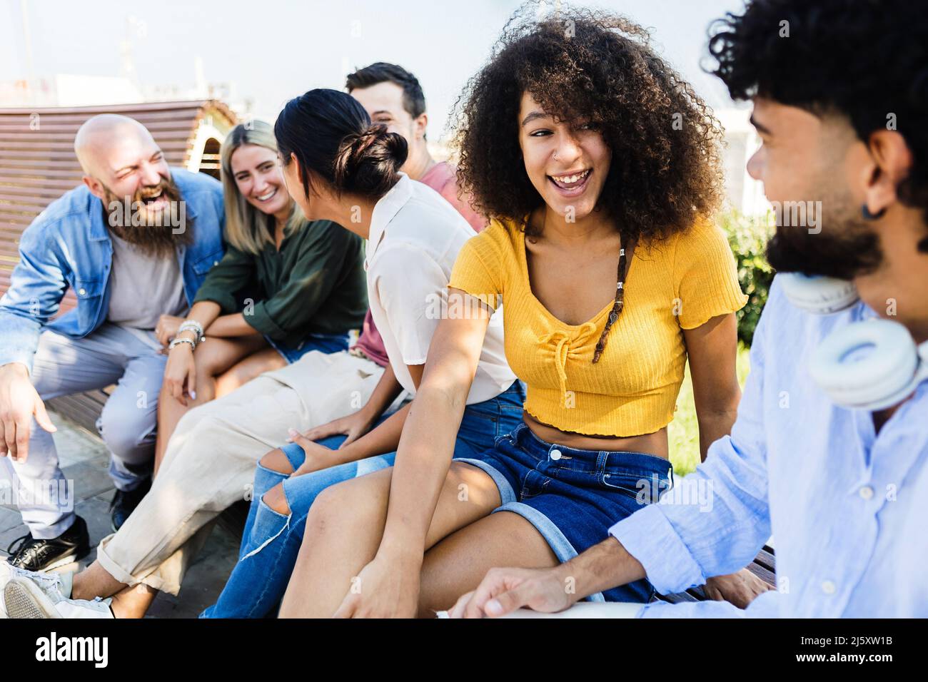 Gruppo di amici studenti che parlano e ridono mentre si siedono insieme all'aperto Foto Stock