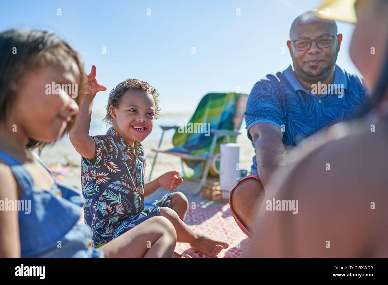Ragazzo felice con sindrome di Down in spiaggia con la famiglia Foto Stock