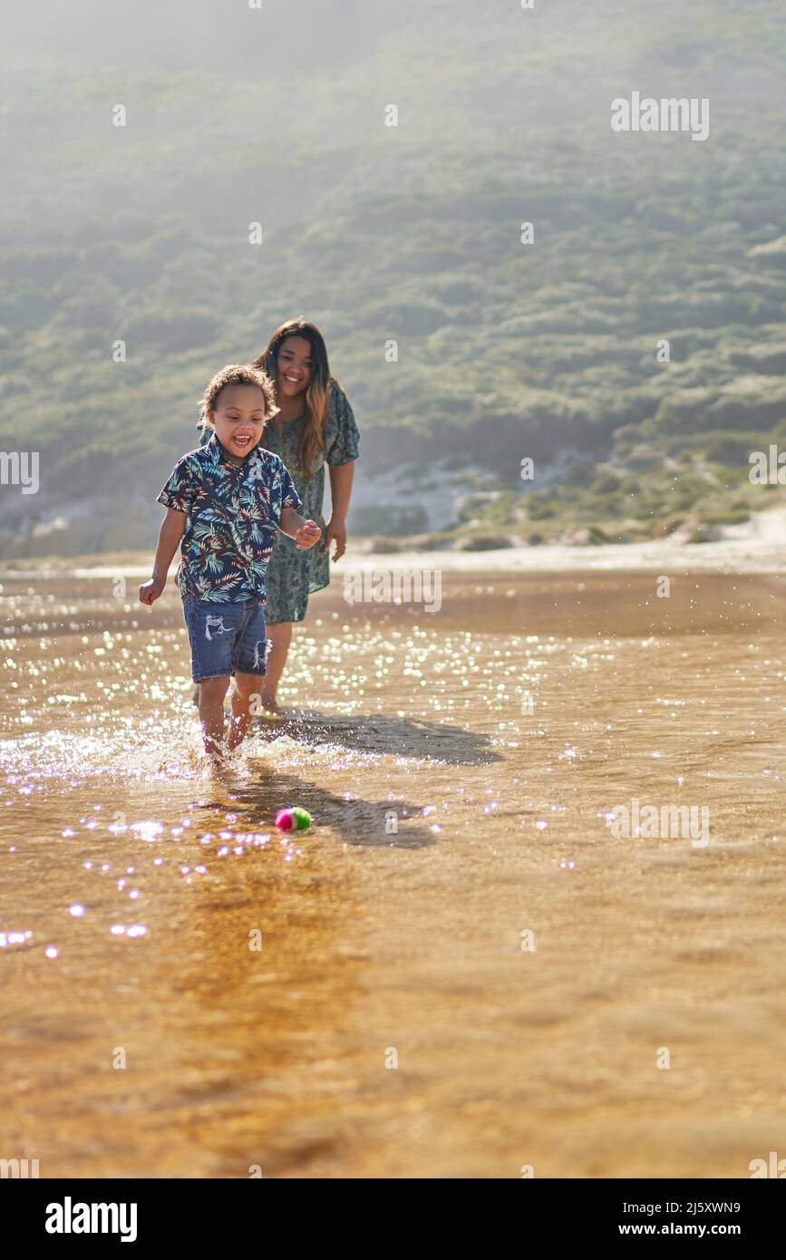 Felice madre e figlio giocare con la palla in mare surf Foto Stock