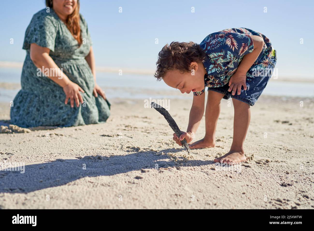 Ragazzo con sindrome di Down disegno in sabbia con bastone su spiaggia soleggiata Foto Stock