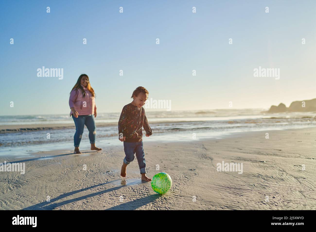 Madre e figlio con la sindrome di Down che gioca con la palla di calcio sulla spiaggia Foto Stock