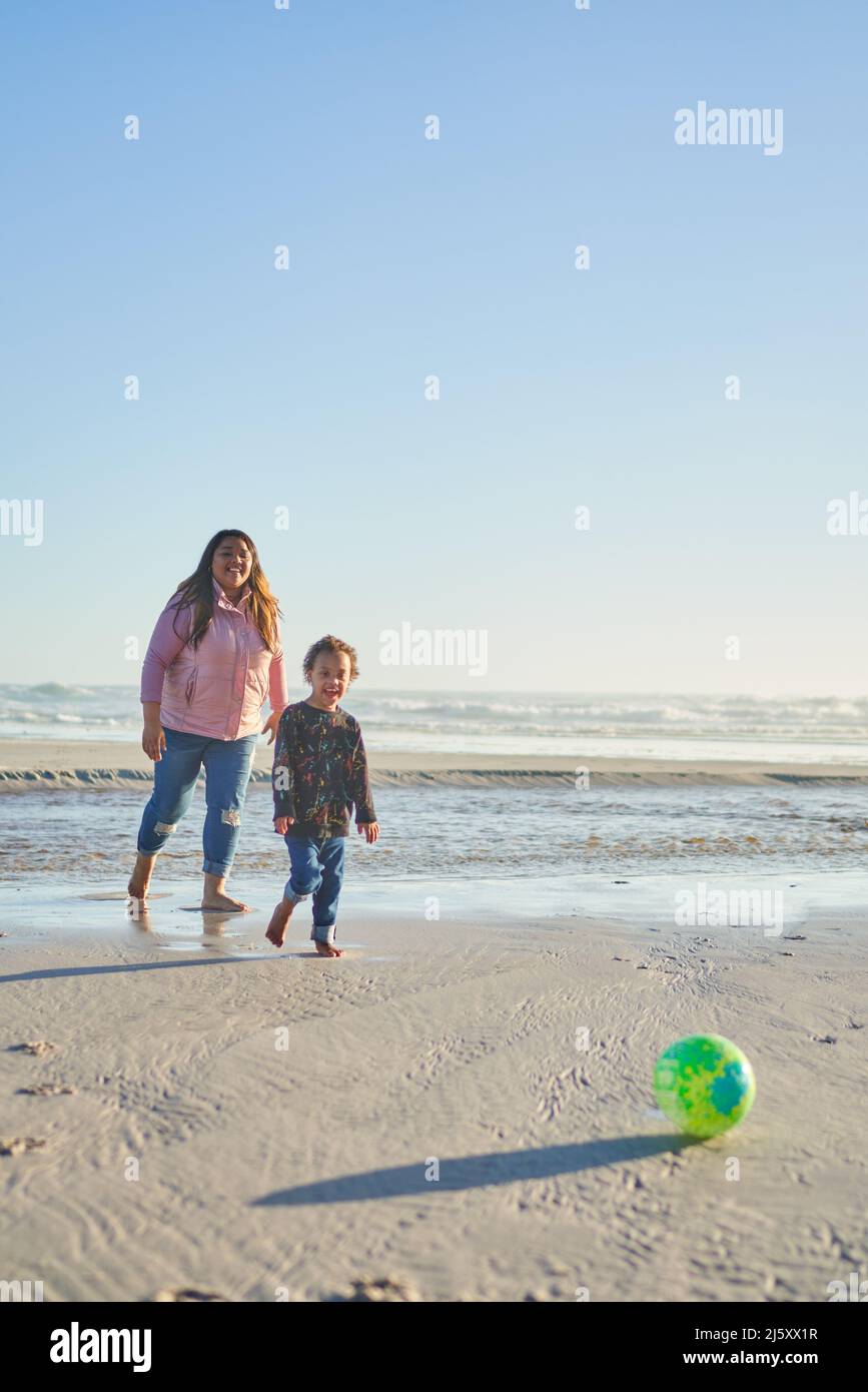 Madre e figlio giocano con la palla di calcio sulla spiaggia soleggiata Foto Stock