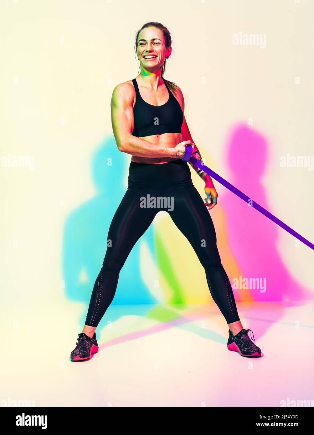 Donna forte che lavora con banda di resistenza. Foto di donna in abbigliamento sportivo nero su sfondo bianco con effetto RGB colori ombre. Sport e salute Foto Stock
