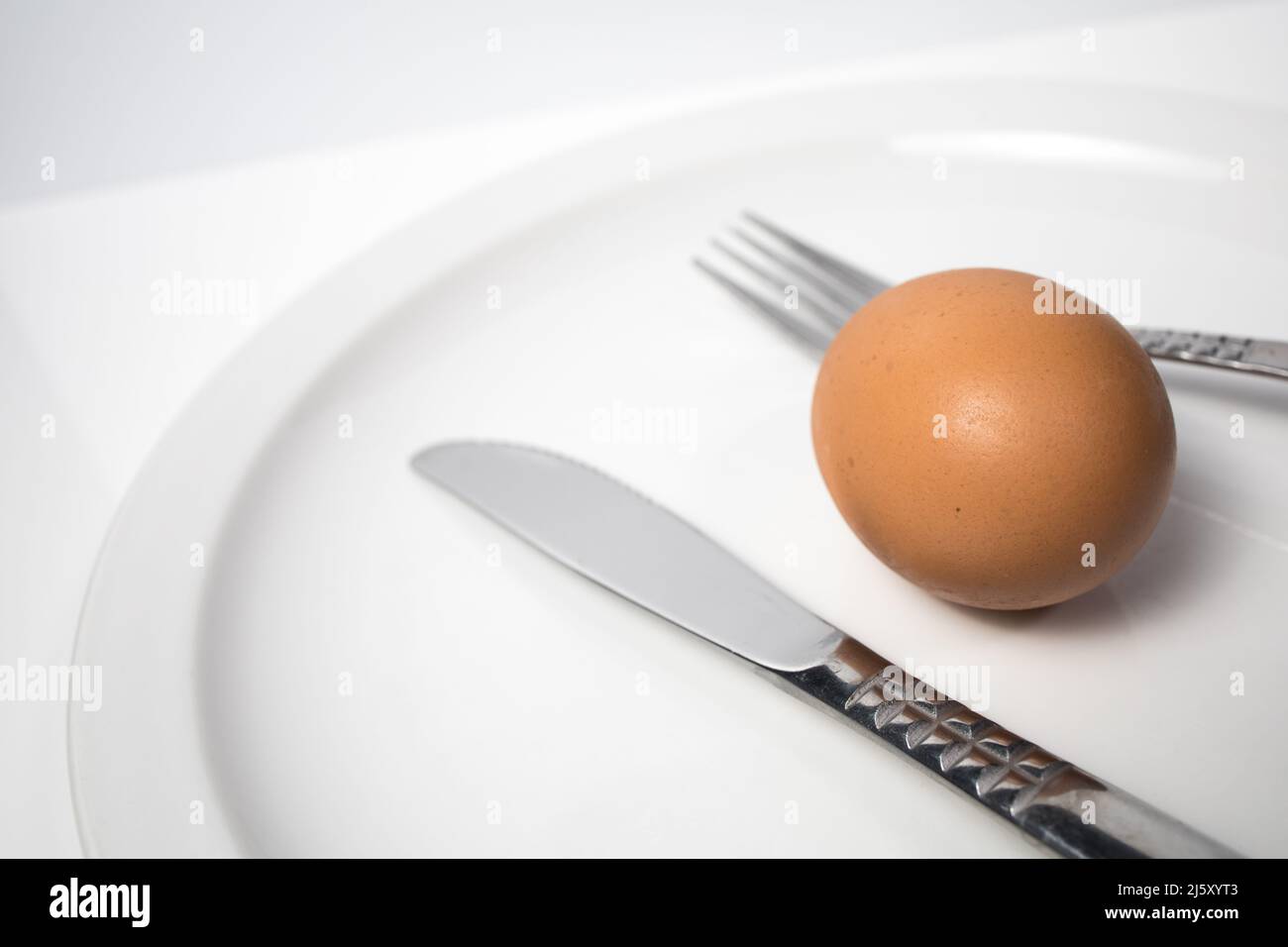 Immagine astratta di un piatto con un uovo e posate su sfondo bianco. Pulire l'immagine di sfondo degli alimenti. Foto Stock