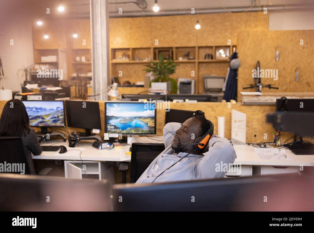 Uomo d'affari in cuffia reclinabile con le mani dietro la testa in ufficio Foto Stock