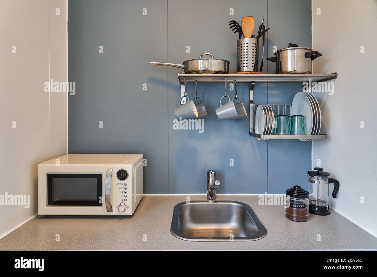 Ripiani con vari utensili e stoviglie appesi a parete sopra il lavandino e  forno a microonde bianco nella cucina luminosa dell'appartamento Foto stock  - Alamy