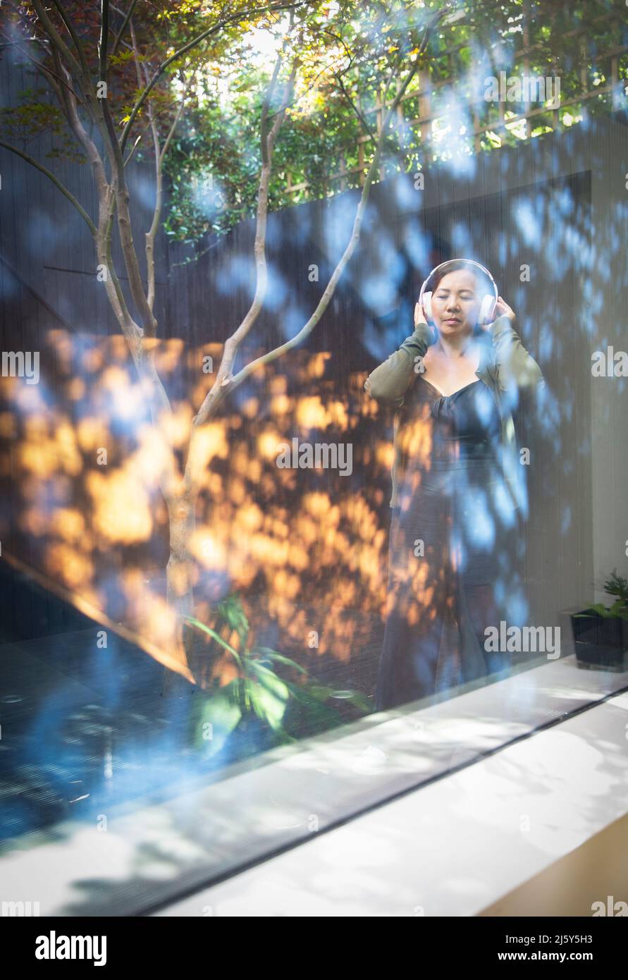 Donna serena che ascolta musica con le cuffie in un cortile soleggiato Foto Stock