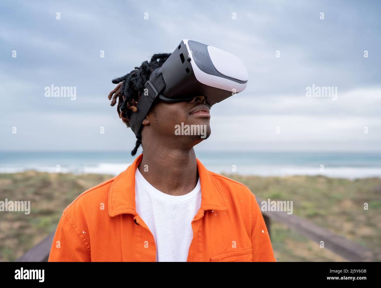 Maschio afro-americano in moderni occhiali di protezione VR esplorare il cyberspazio mentre si trova sul lungomare sulla costa vicino al mare e la mano stretching Foto Stock