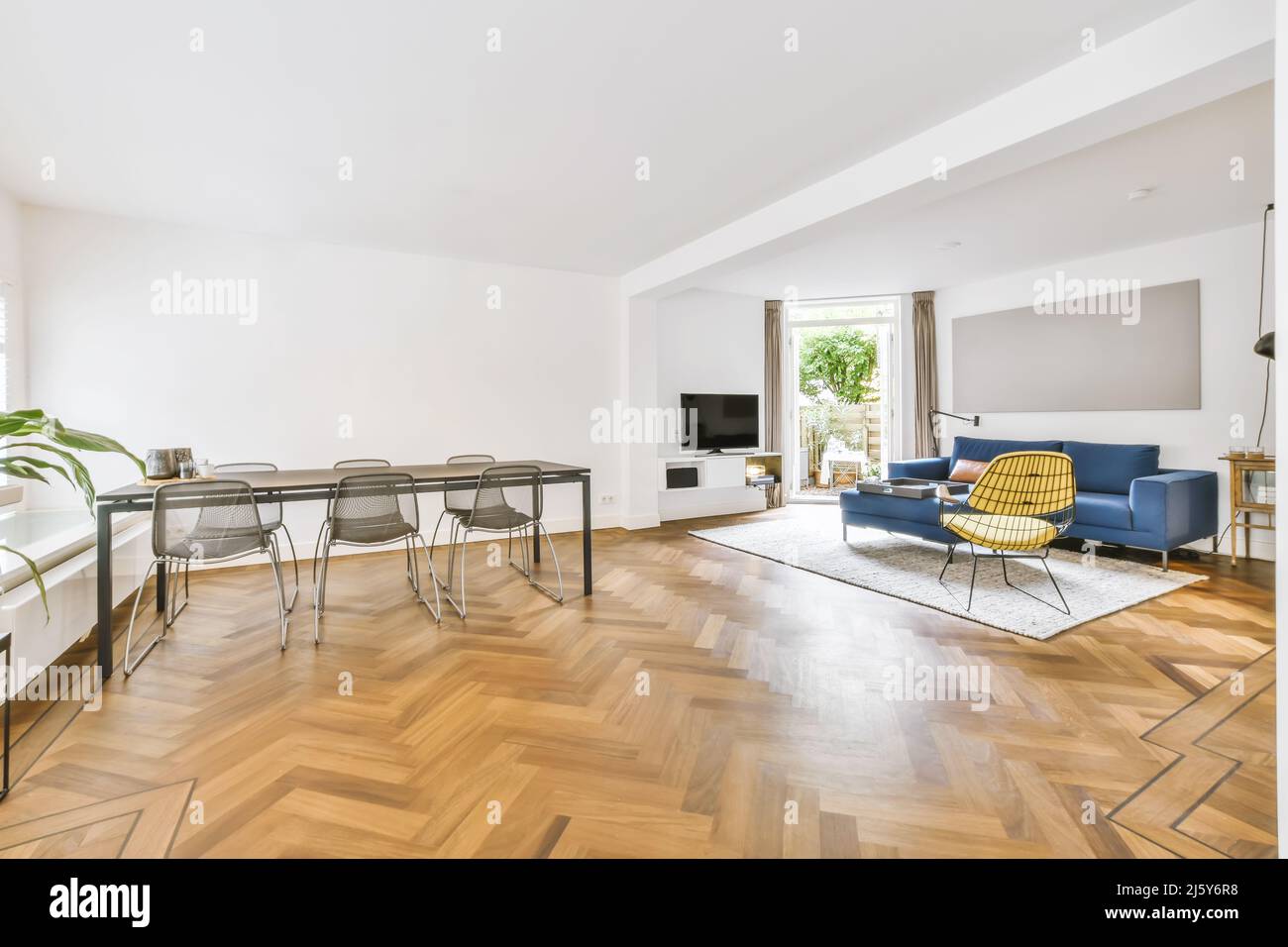 Sedie al tavolo da pranzo collocato in un ampio e luminoso soggiorno con comodo divano e TV in elegante appartamento con finestra Foto Stock