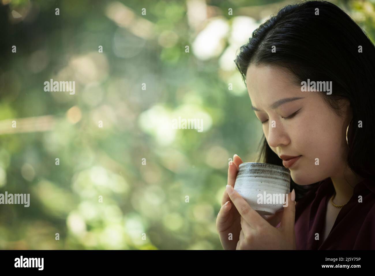 Giovane donna serena che beve il tè alla finestra Foto Stock