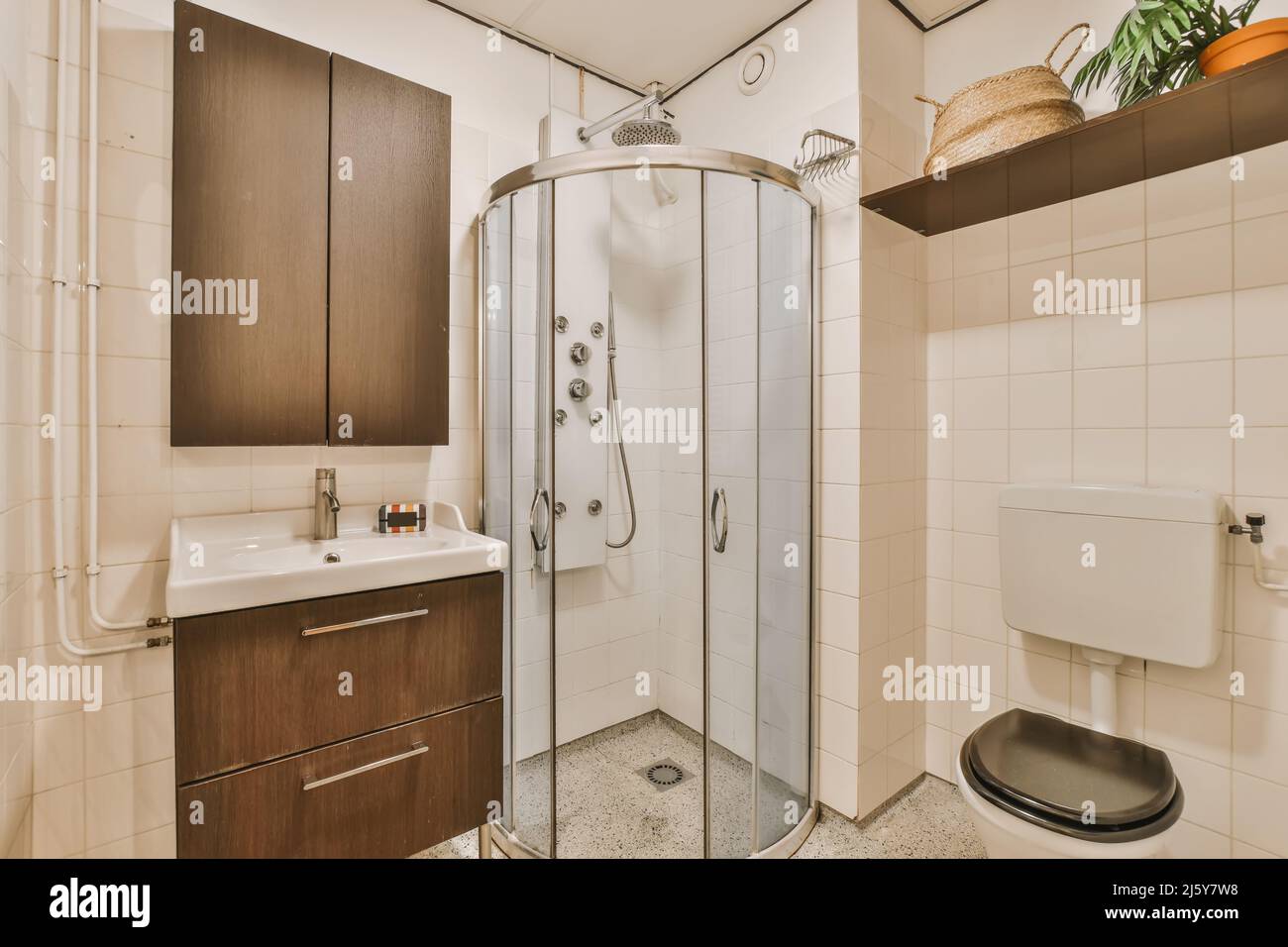Interno di moderno bagno luminoso con cabina doccia e wc vicino lavandino sotto armadio in appartamento Foto Stock