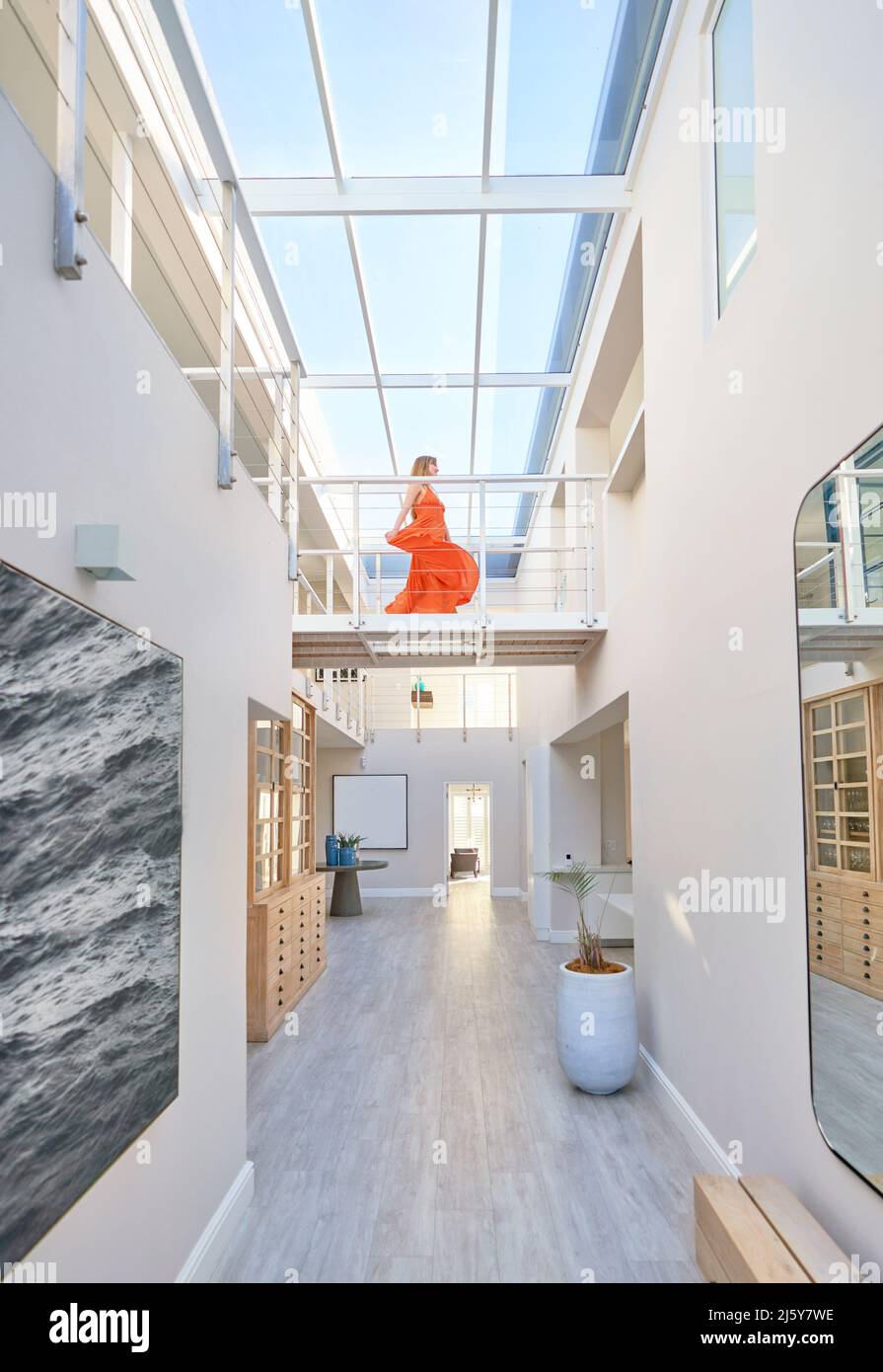 Donna in abito arancione che cammina attraverso la passerella in casa moderna Foto Stock